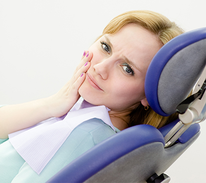 Woman in dental chair holding cheek