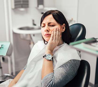 Woman in dental chair holding jaw